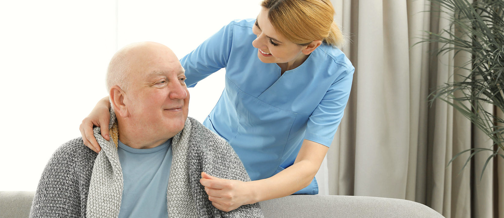 Caregiver touching elderly man shoulder on couch